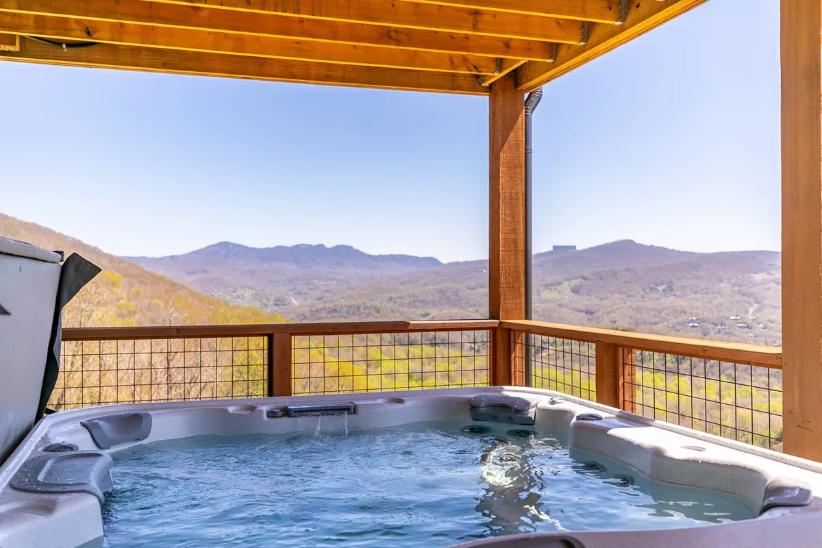 This serene image highlights the lower deck's spa-like hot tub, framed by a wooden railing and structure, overlooking gorgeous mountain scenery. The tranquil mood evokes relaxation and the pleasures of soaking in the hot tub while taking in the view.
