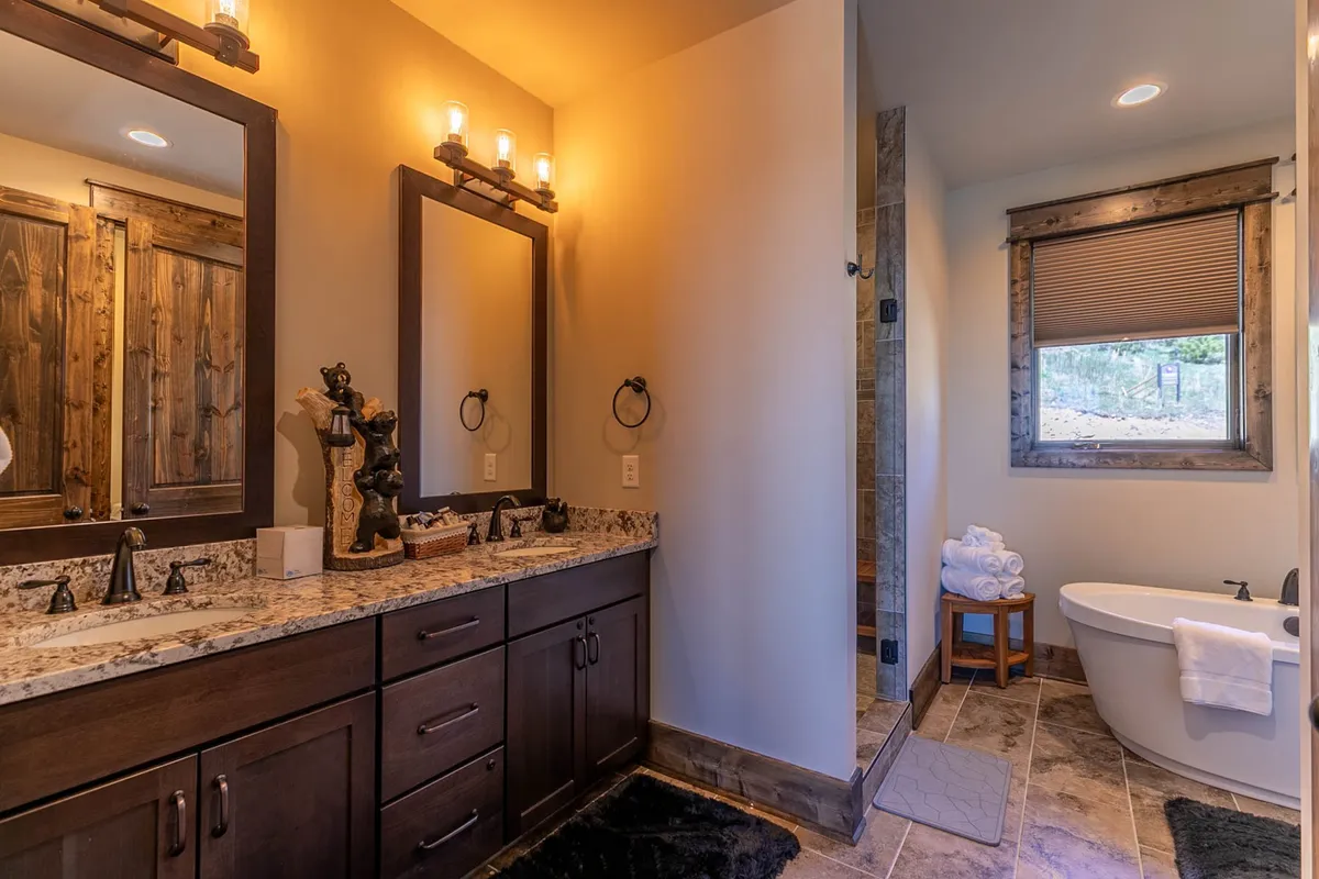 A spacious bathroom with a double vanity, freestanding bathtub, large mirrors, and a granite countertop. Natural light fills the space, creating a serene and luxurious environment ideal for self-care and relaxation.