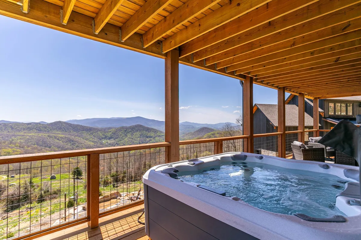 An exterior shot of a hot tub on a wooden deck with stunning mountain views. The scene highlights the peaceful atmosphere and proximity to nature, suggesting easy access from the lower level den to the outdoor hot tub—a key convenience mentioned in the section.