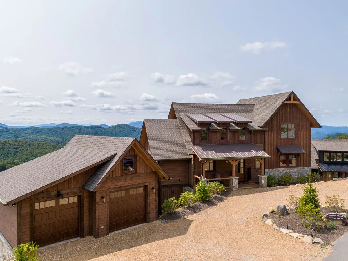 A welcoming view of the house exterior shows wooden facades, prominent garage doors, a landscaped driveway, and a scenic mountain vista in the background. The porch invites gatherings and relaxation, emphasizing a sense of home base at the heart of exploration.