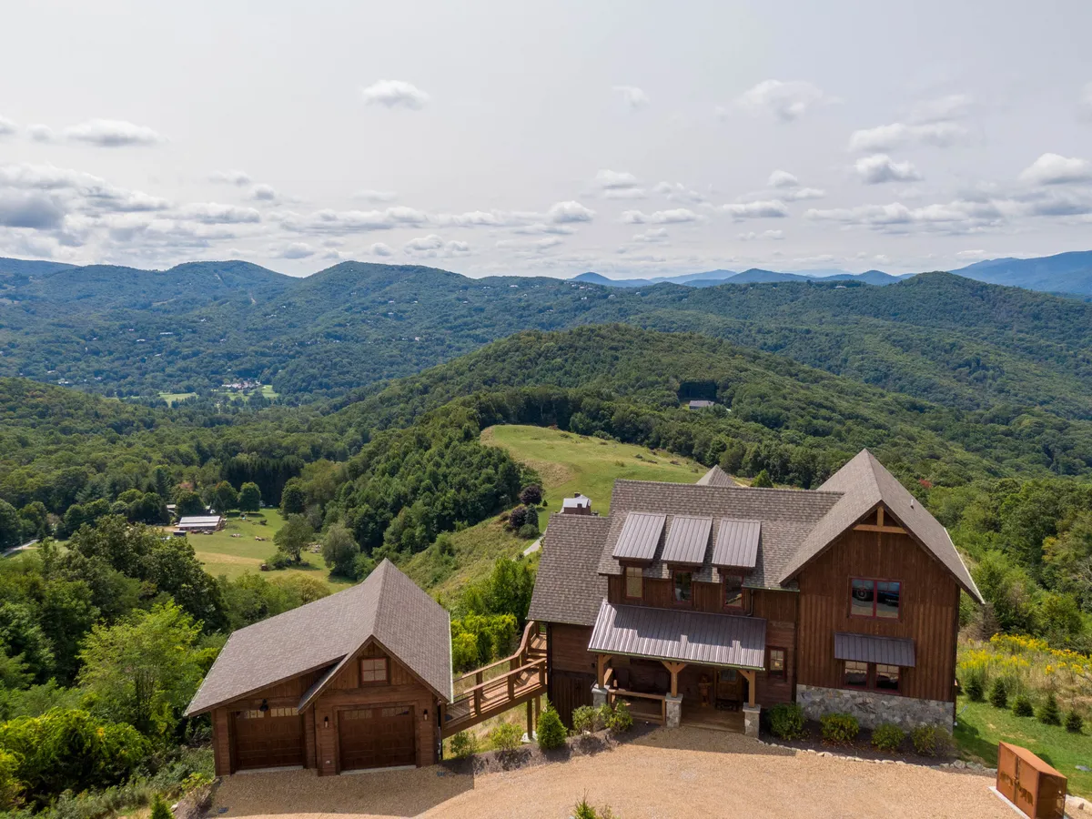 This exterior image features the wooden house nestled in lush greenery, with a striking view of the surrounding mountain range and a visible driveway that hints at adventure and exploration right from the doorstep. The setting evokes a sense of being immersed in nature and serves as a visual gateway to local trails and outdoor activities.