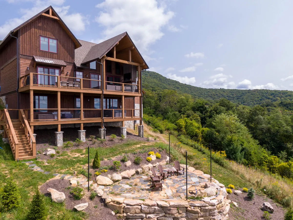 An inviting outdoor deck and stone patio overlook a scenic mountain view and landscaped garden. The space includes areas for relaxing by the fire pit, outdoor dining, and stargazing—ideal for unwinding after a day of adventure or gathering with friends.